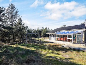 Una casa moderna con un invernadero de vidrio, un columpio y una terraza de madera.