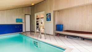 Una piscina con una escalera metálica, una puerta y una cesta azul en el suelo.