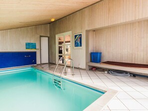 Una piscina con una escalera metálica, una puerta y una cesta azul en el suelo.