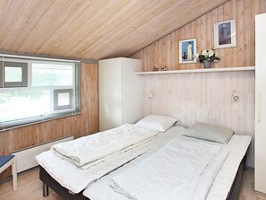 A bedroom with a wooden ceiling, a bed with white bedding, a bedside table, and a window with blinds. - 4 Star Holiday Home in Albaek (Aalbaek)