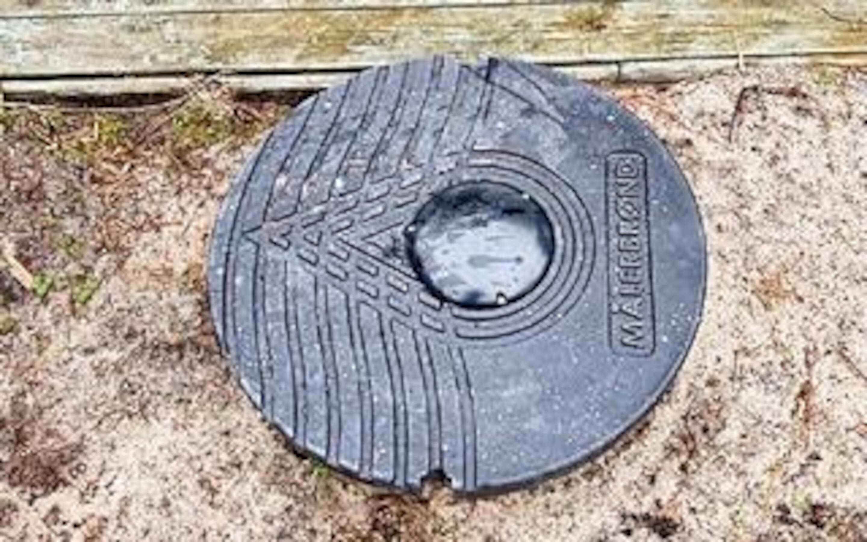 A circular metal object with a textured surface and a central hole, placed on sandy ground.