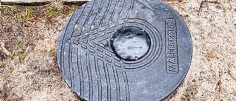 A circular metal object with a textured surface and a central hole, placed on sandy ground.
