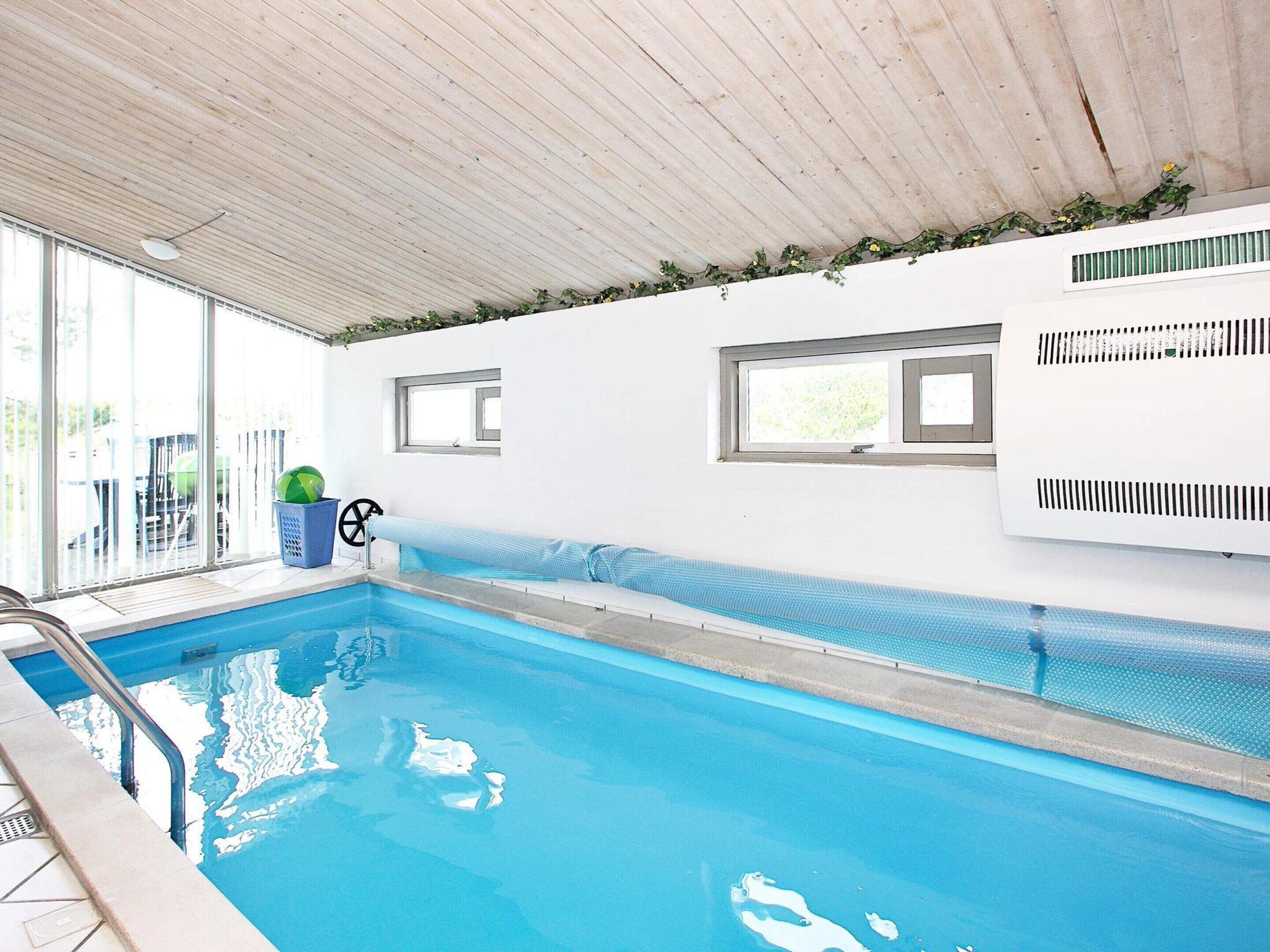 Una piscina interior con agua azul cristalina, techo de madera y un banco a lo largo de la pared.