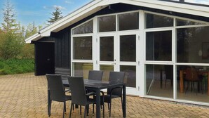 A modern house with a large glass door and a patio with a table and chairs. - 5 Star Holiday Home in Lokken (Lokken)