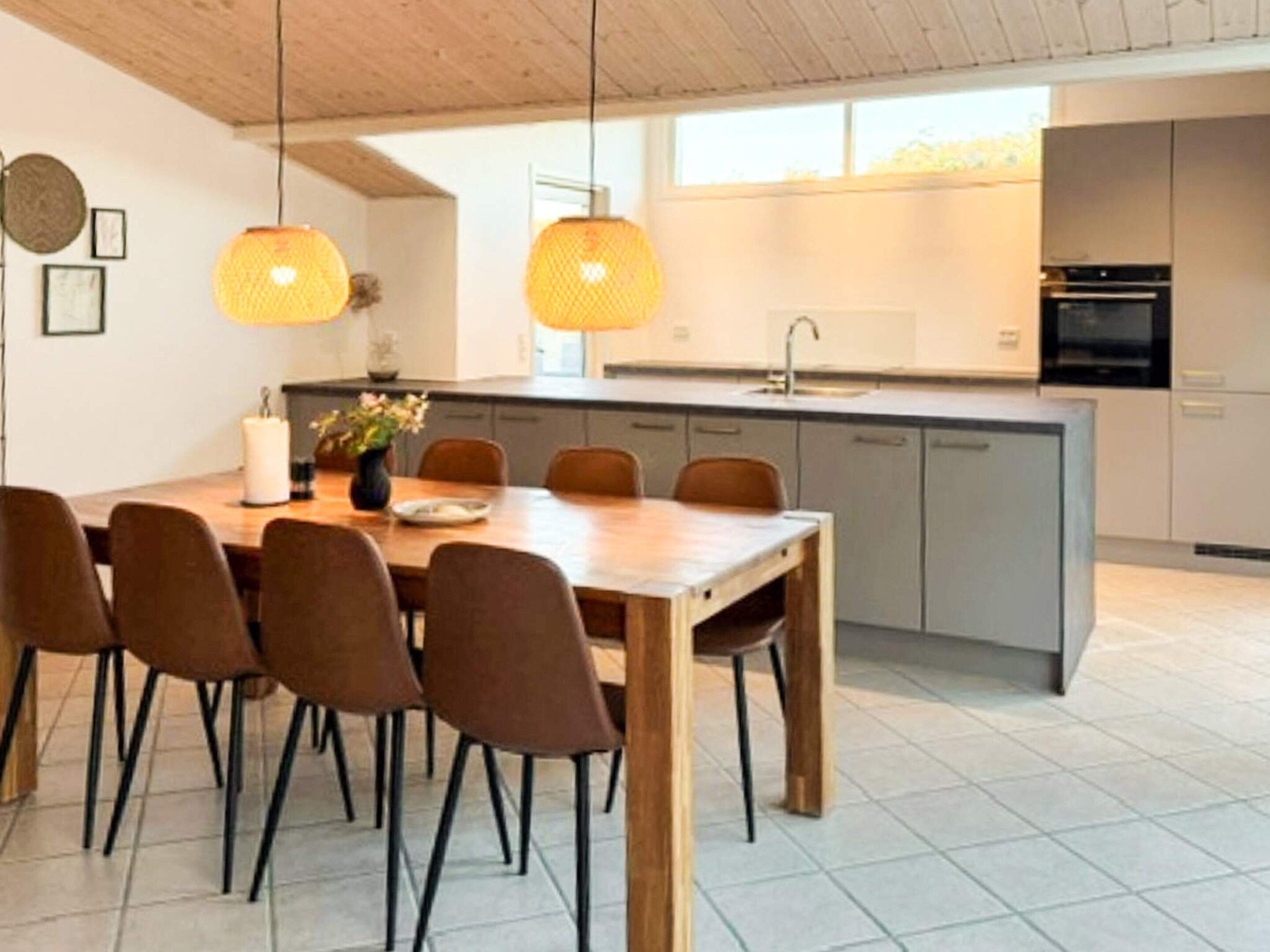 A modern kitchen with a central island, pendant lighting, and a dining area with chairs and a table.
