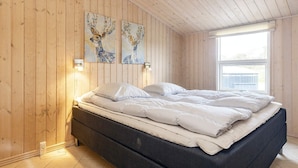 A bedroom with wooden walls, a bed with white bedding, and two wall-mounted paintings. - 5 Star Holiday Home in Lokken (Lokken)