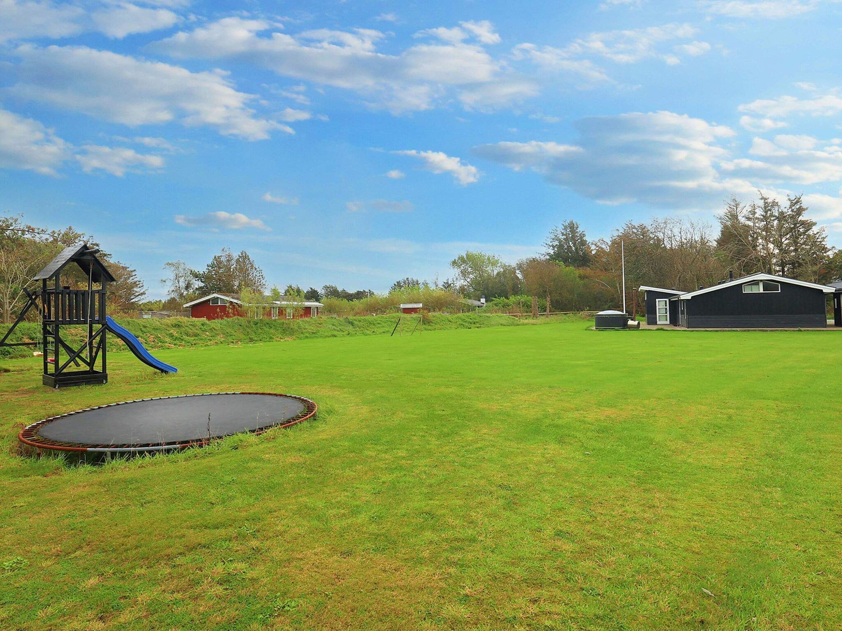 A grassy yard with a trampoline, a play structure, and a small shed.