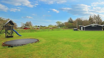 A grassy yard with a trampoline, a play structure, and a small shed.