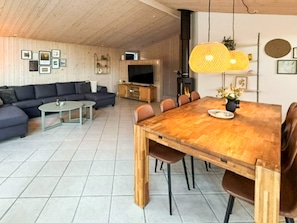 A modern living room with a wooden dining table, a sofa, and a television. - 5 Star Holiday Home in Lokken (Lokken)