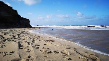 A sandy beach with footprints, a cliff, and waves in the background.