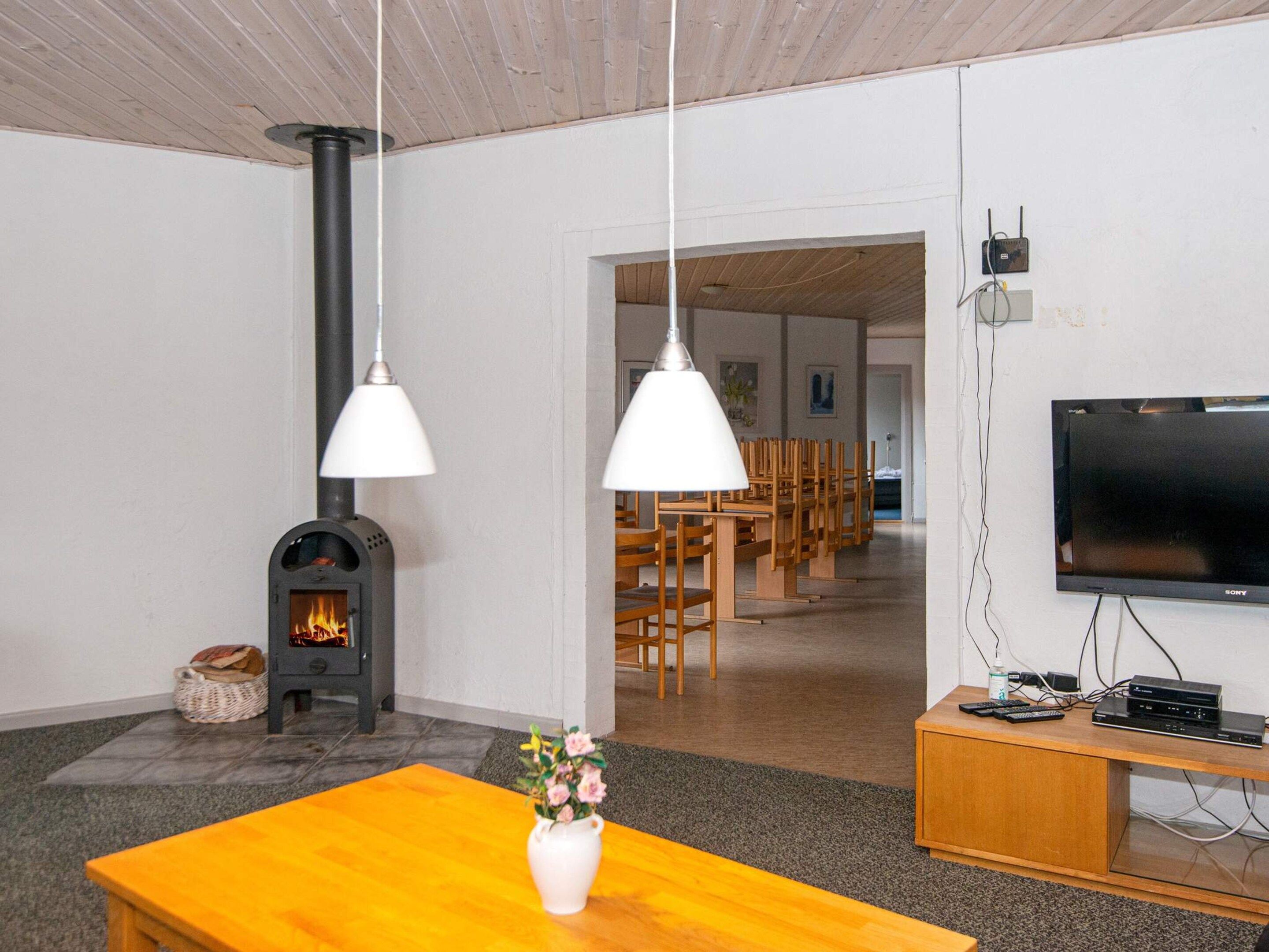 A living room with a fireplace, wooden furniture, a television, and hanging pendant lights.