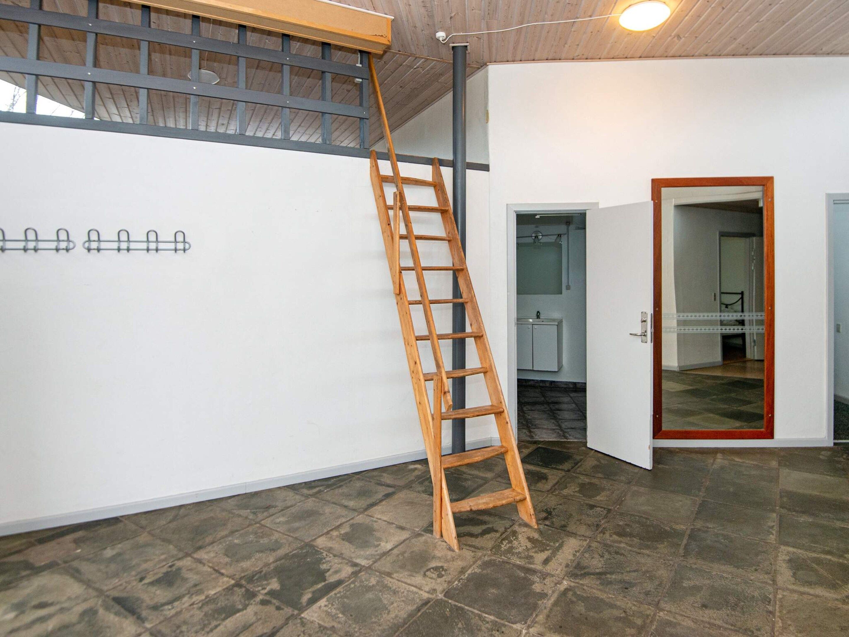 A room with a wooden ladder leaning against a wall, a tiled floor, and a door leading to another room.