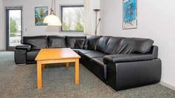 Ein Wohnzimmer mit einem schwarzen Ledersofa, einem Holztisch und einer Stehlampe.