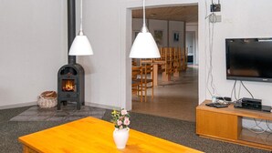 Una sala de estar con chimenea, muebles de madera, un televisor y un comedor al fondo.