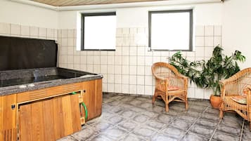 Ein Zimmer mit einem Holzkabinett, zwei Korbstühlen, einer Topfpflanze und einem Fliesenboden.