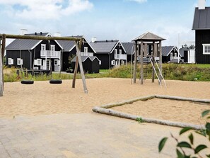A playground with swings and tire swings, surrounded by black wooden houses with white trim. - 8 Person Holiday Home in Gjern-by Traum (Gjern)