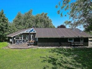 Eine Holzhütte mit geneigtem Dach, einer überdachten Veranda mit Stühlen und Blick auf den umliegenden Wald.