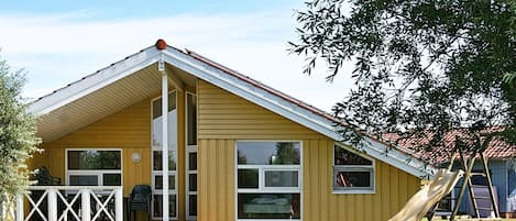 A yellow building with a gabled roof, large windows, and a slide in the yard.