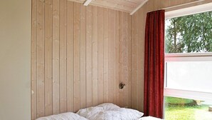 A room with a wooden paneled wall, a bed with white bedding, and a window with red curtains. - Holiday Home in Otterndorf (Otterndorf)