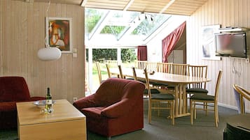 Una habitación con techo de madera, una mesa de comedor con sillas, un sofá, un televisor y una ventana con cortinas.