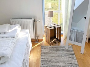 A bedroom with a bed, a radiator, a window with curtains, a lamp on a wooden stand, and a mirror. - Holiday Home in TvÃ¥Ã¥ker (Tvaaker)