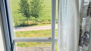 Ett fönster med utsikt över ett lantligt landskap, inklusive ett träd och en grusväg.