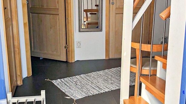 En trappa med trästeg och ett ledstång, som leder upp till en liten plattform med en spegel och en dörr.