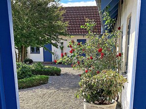 Une cour avec un chemin de gravier menant à un bâtiment dont le toit est recouvert de tuiles rouges.