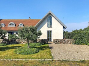 Une maison à deux étages, avec un toit en pente, un mur en pierre et une allée gravillonnée.