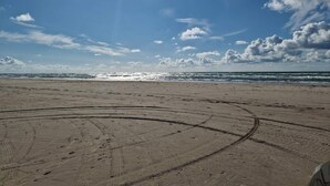 A beach with tire tracks leading to the water, a clear sky, and the sun shining. - 4 Star Holiday Home in Blokhus (Blokhus)