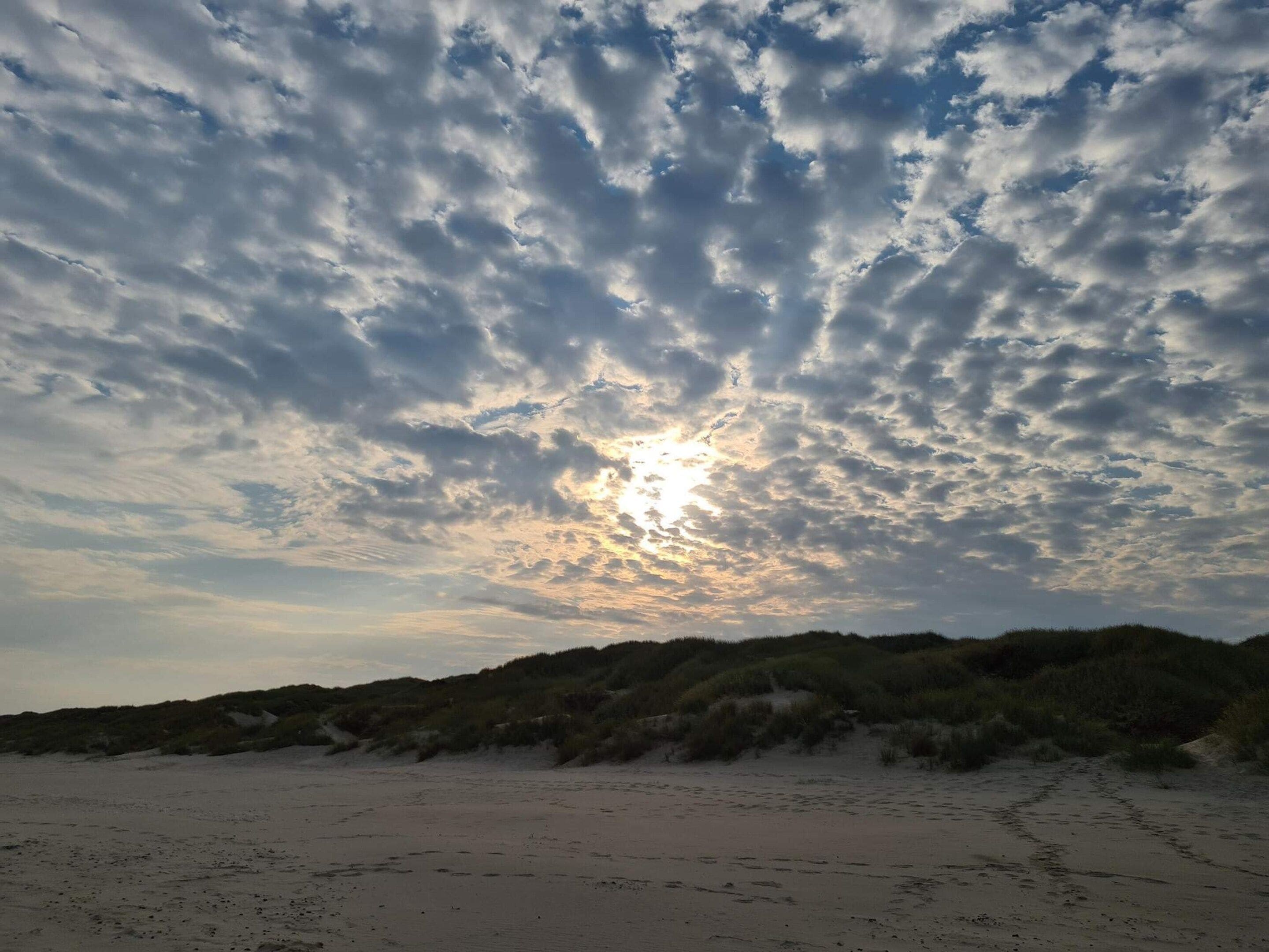 A beach with sand and dunes under a cloudy sky.