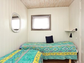A room with two beds, a window with blinds, a wall-mounted mirror, and a bedside lamp.