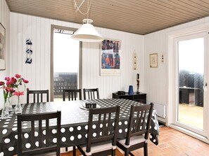 A dining area with a round table, chairs, a hanging light fixture, and a view through a glass door.
