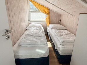 A small, single-room accommodation with two beds, a window with curtains, and a door with a handle. - Holiday Home in Otterndorf (Otterndorf)