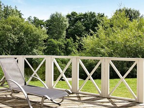 A wooden deck with a white railing, a single lounge chair, and lush greenery in the background. - Holiday Home in Otterndorf (Otterndorf)