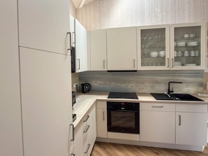 A modern kitchen with white cabinets, a black countertop, a built-in oven, and a dishwasher. - Holiday Home in Otterndorf (Otterndorf)