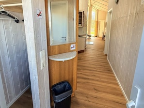 A narrow hallway with wooden walls, a mirror, a small sink, and a trash bin. - Holiday Home in Otterndorf (Otterndorf)