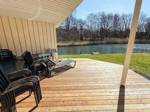A covered outdoor deck with a table and chairs, a grill, and a view of a lake. - Holiday Home in Otterndorf (Otterndorf)