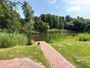 A wooden dock extending into a calm pond surrounded by lush greenery. - Holiday Home in Otterndorf (Otterndorf)