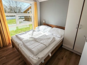A bedroom with a bed, wooden headboard, and a window with curtains. - Holiday Home in Otterndorf (Otterndorf)