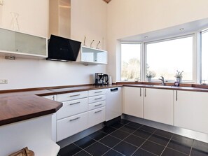 A modern kitchen with white cabinets, a black tiled floor, a built-in oven, a coffee maker, and a window providing natural light.