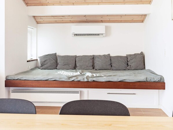 A compact room with a bed, a window, an air conditioning unit, and a desk with chairs.