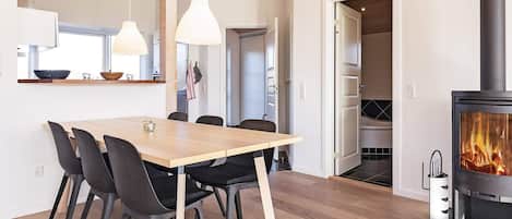 A modern kitchen with a wooden dining table, chairs, pendant lights, and a visible fireplace.
