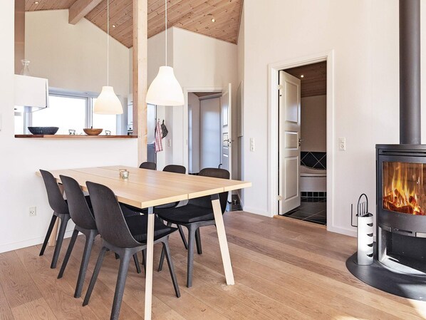 Une cuisine moderne avec une table à manger en bois, des chaises, des luminaires suspendus et une cheminée visible.