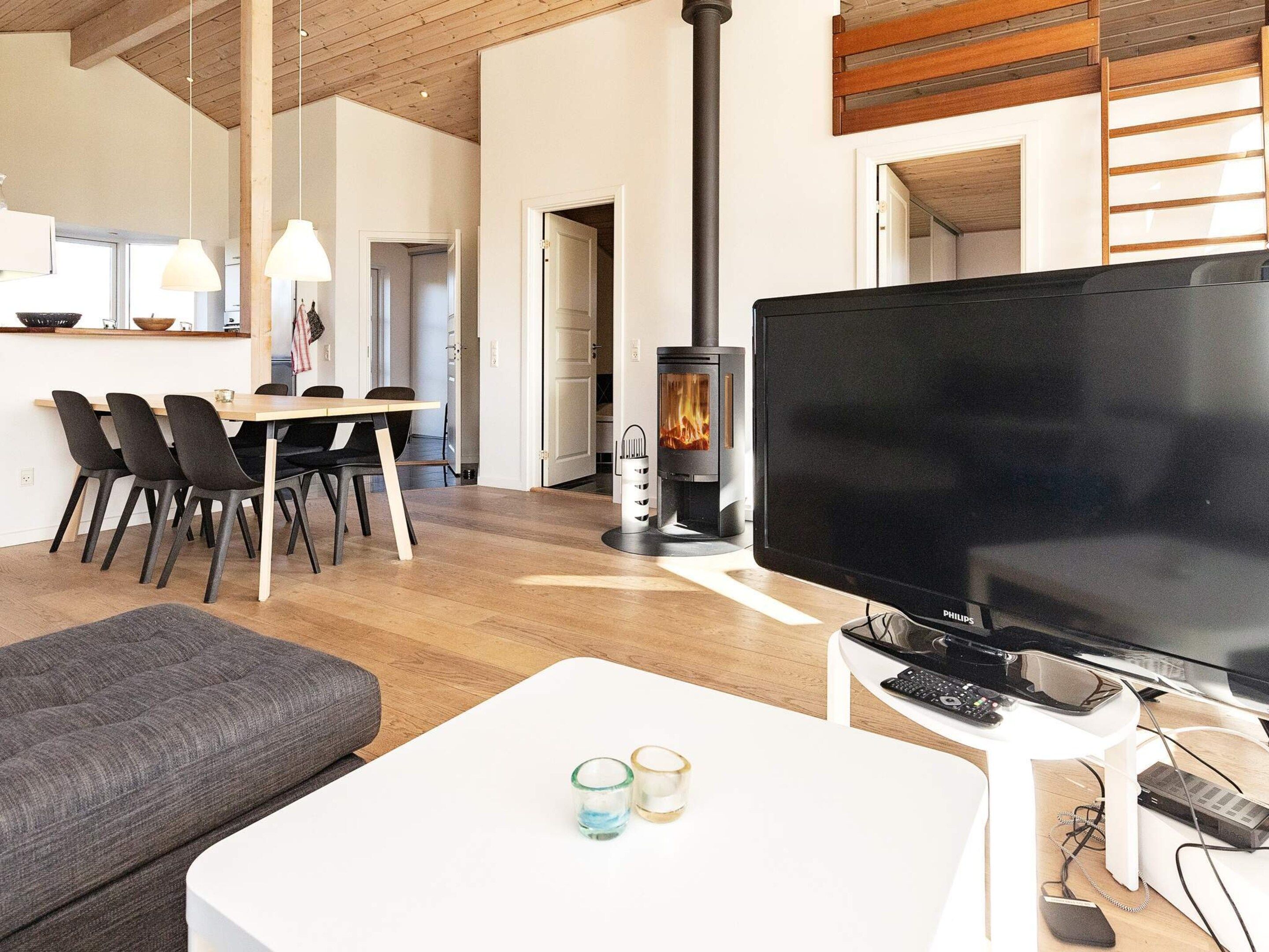 Ein modernes Wohnzimmer mit Flachbildfernseher, Kamin, Essbereich mit Stühlen und einer Couch.