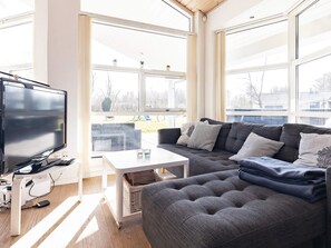 Un salon moderne avec un grand téléviseur à écran plat, un canapé gris et une table basse blanche.