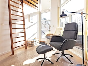 A modern room with a wooden ladder, a grey office chair, a floor lamp, and a large window with a view of trees.