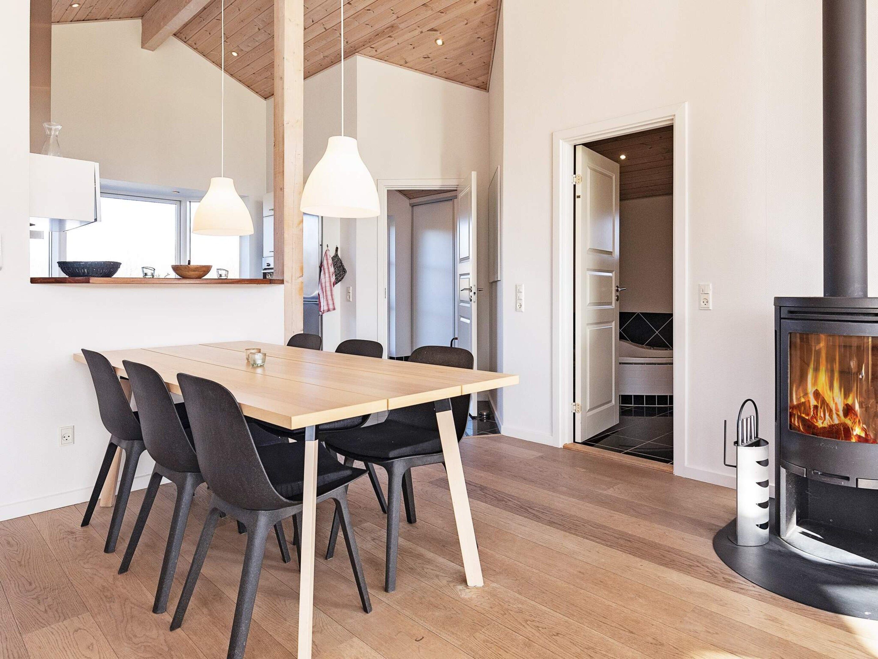 Et moderne køkken med et træbord og stole, en hængende lampe og en synlig pejs.