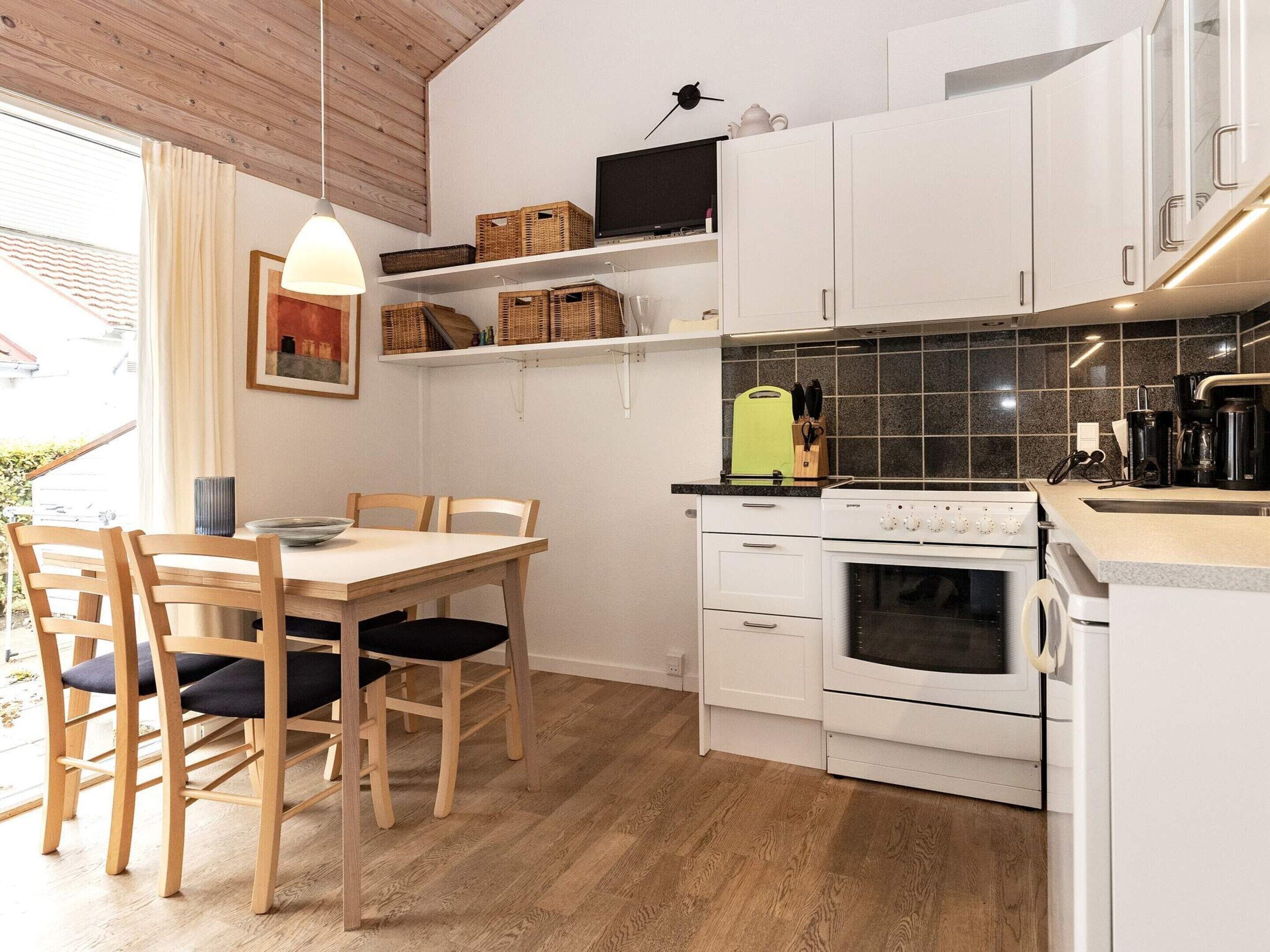 A modern kitchen with white cabinets, a built-in oven, and a dining area with wooden chairs and a table.