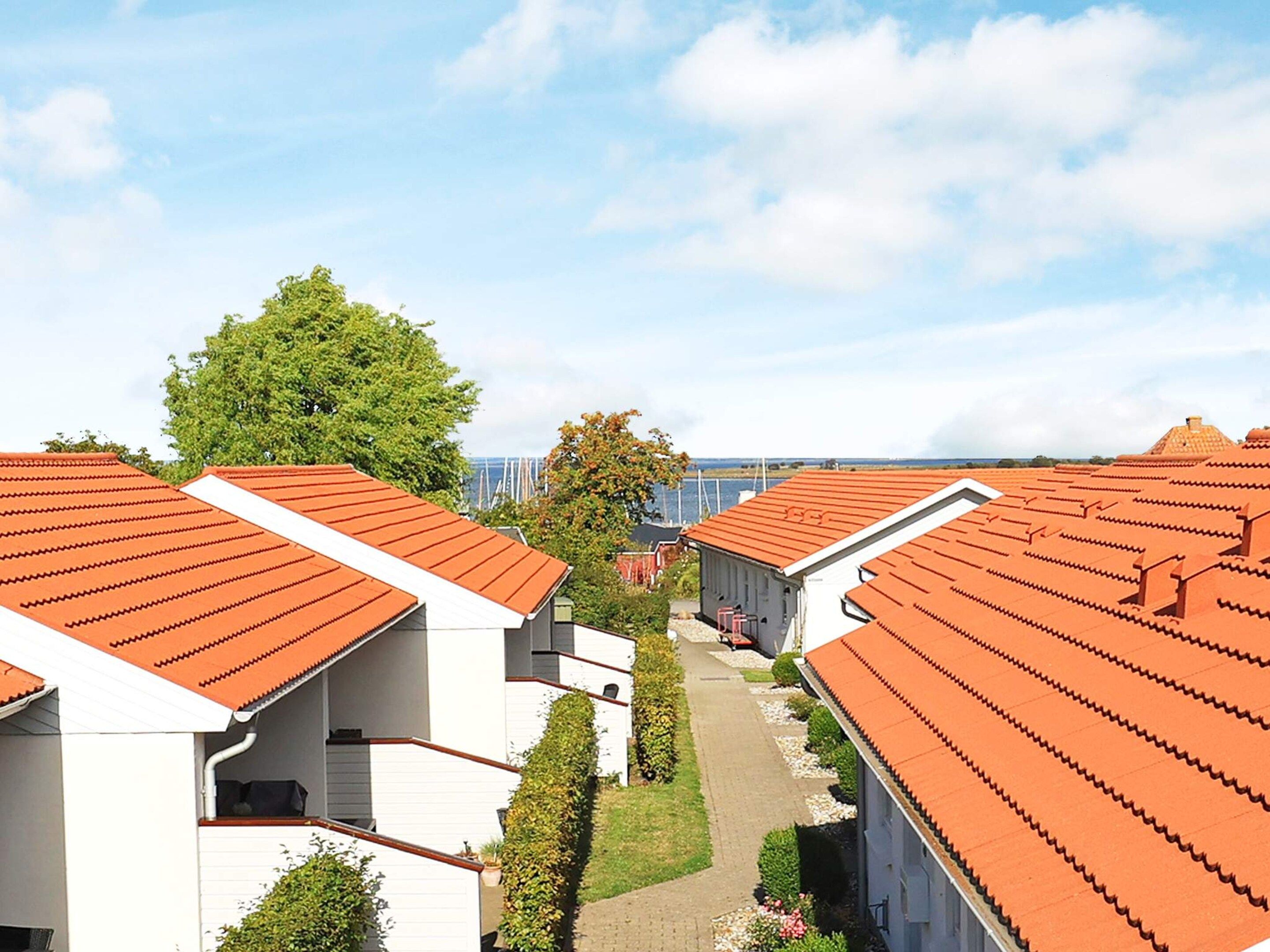 A row of modern buildings with red-tiled roofs and white walls, arranged in a linear fashion with a pathway between them.